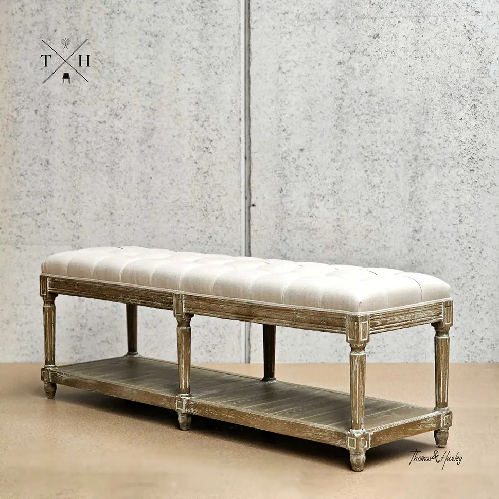 Ottoman with natural upholstery placed at the foot of a Hamptons style bed